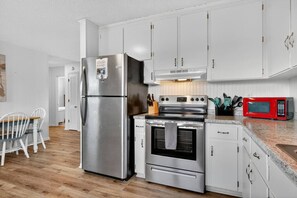 A modern kitchen with stainless steel appliances, white cabinetry, and a granite countertop. - UNIT A: Walk to Beach/Intercoastal/Fishing Pier. Drive to Golf/Deep Sea Fishing (Holly Ridge)