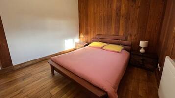 Een slaapkamer met een houten vloer, een bed met roze beddengoed, twee bedlampjes en een nachtkastje.