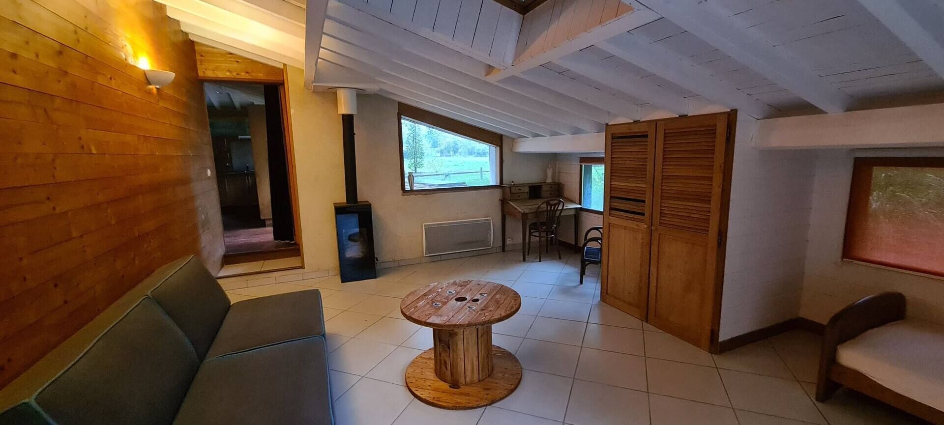 A cozy room with a wooden bench, a round wooden table, a window with a view, and a door leading to another room.