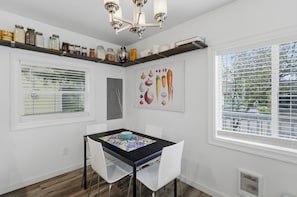 Ein Essbereich mit Tisch, Stühlen, einer Chandelieber, einem Fenster mit Jalousien und einem an der Wand befestigten Regal mit Gläsern.