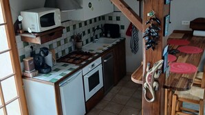 Een kleine keuken met rieten dak, een magnetron, een spoelbak en een eethoek met tafel en stoelen.