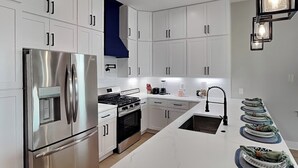 Una cocina moderna con armarios blancos, electrodomésticos de acero inoxidable, una isla central y una pared de acento azul.