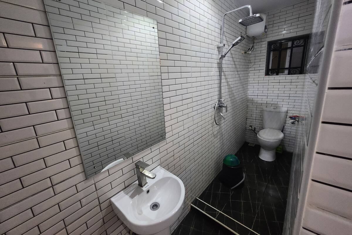 Ein Badezimmer mit weißen Fliesen, einem weißen Waschbecken, einer Dusche und einer Toilette.