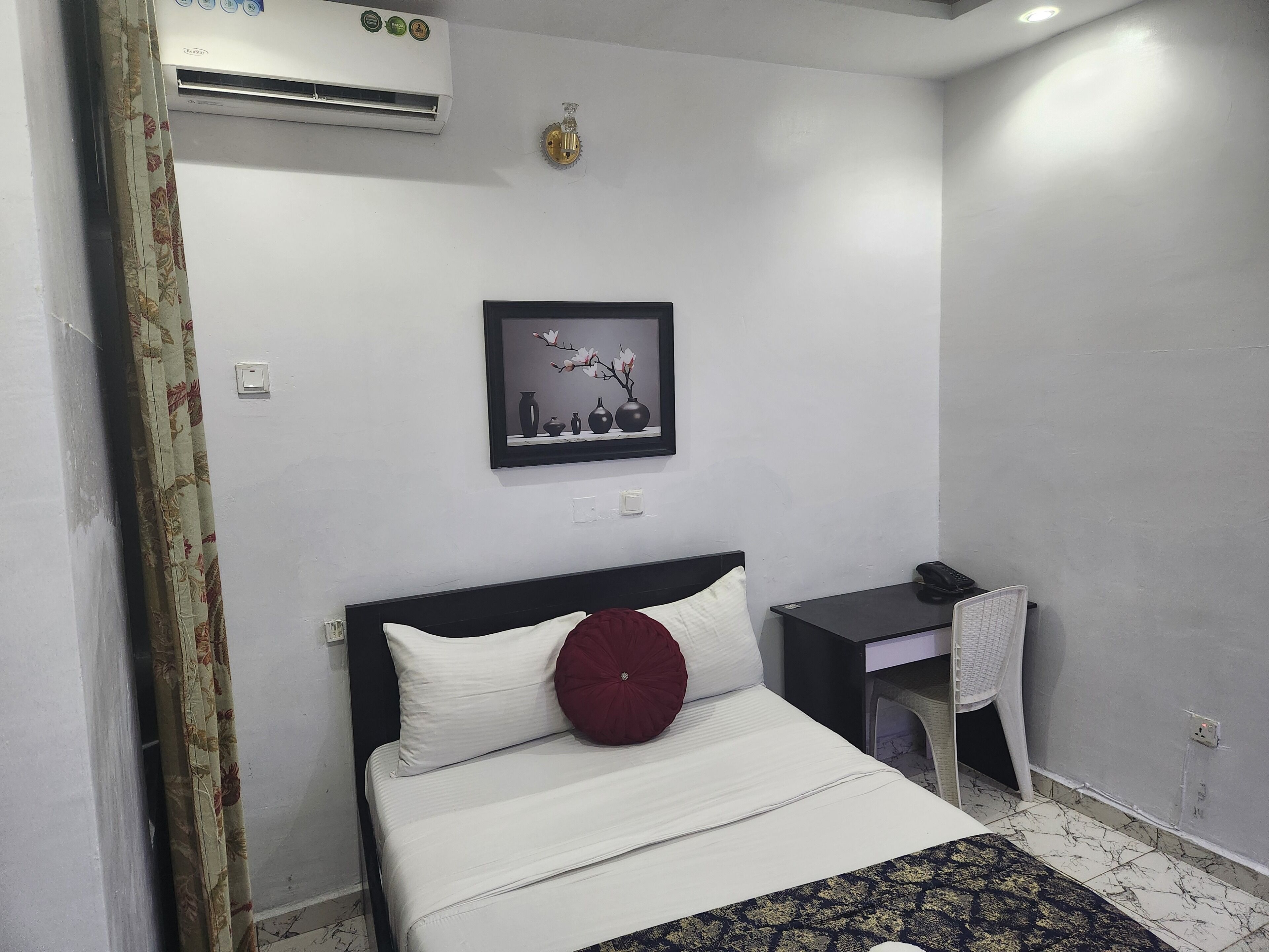 Une chambre d’hôtel équipée d’un lit, d’un bureau, d’un climatiseur, d’un tableau encadré et d’un téléphone.
