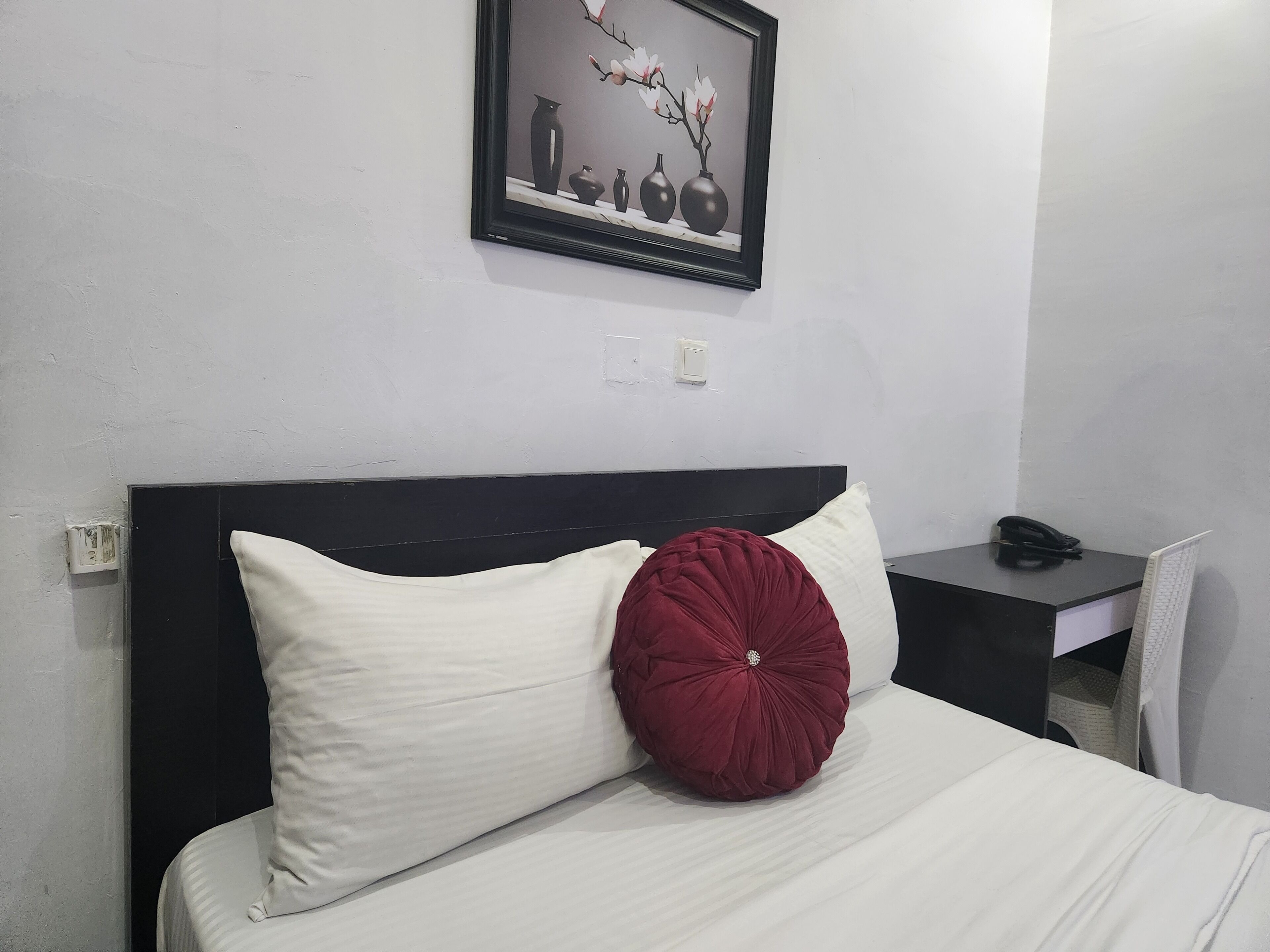 Habitación de hotel con cama, mesita de noche, escritorio y un cuadro en la pared.