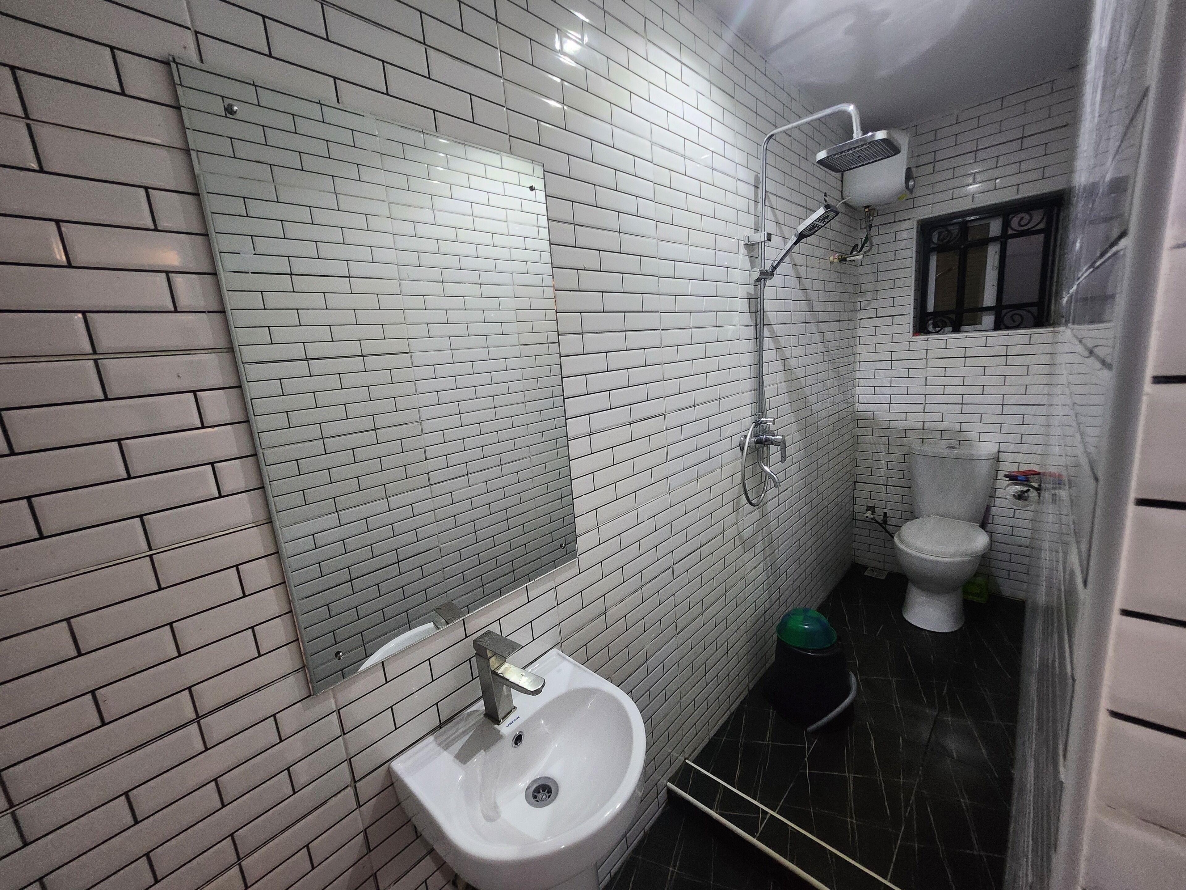Un baño con paredes de azulejos blancos, un lavamanos blanco, un inodoro y una ducha.