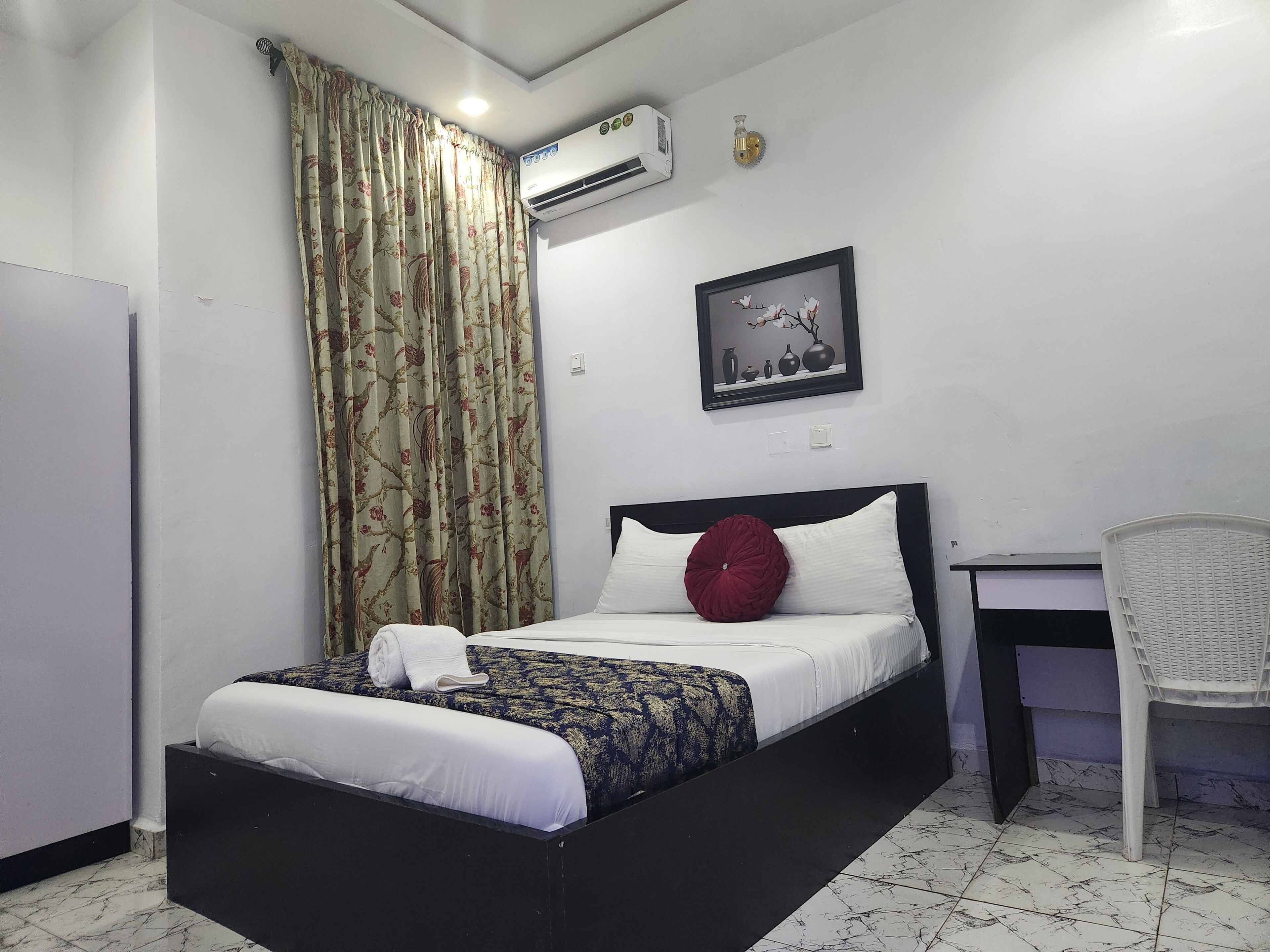 Habitación de hotel con cama, escritorio, aire acondicionado, un cuadro enmarcado y una cortina.