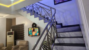 Un escalier avec une rampe en métal, un téléviseur à écran plat fixé au mur et un luminaire au plafond.