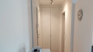 Un corridoio con pavimento in legno, parete bianca, un orologio e una porta in fondo.