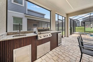 Eine Außenküche mit Grill, Spüle und integriertem Schrank, neben einer Terrassenfläche mit Tisch und Stühlen.