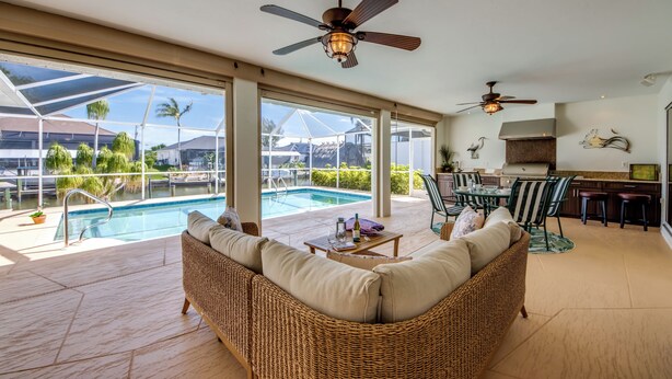A spacious indoor area with a pool, wicker furniture, ceiling fans, and a kitchen area. - Tropical Tiki, Heated Pool, Waterfront Gulf Access, Dock your boat, WIFI (Cape Coral)