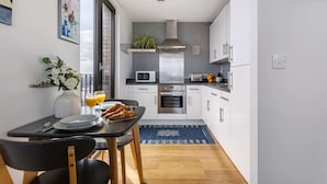 Et moderne køkken med hvide skabe, en mikrobølgeovn, ovn og en vask. Der er et spisebord med stole og en vase med blomster.
