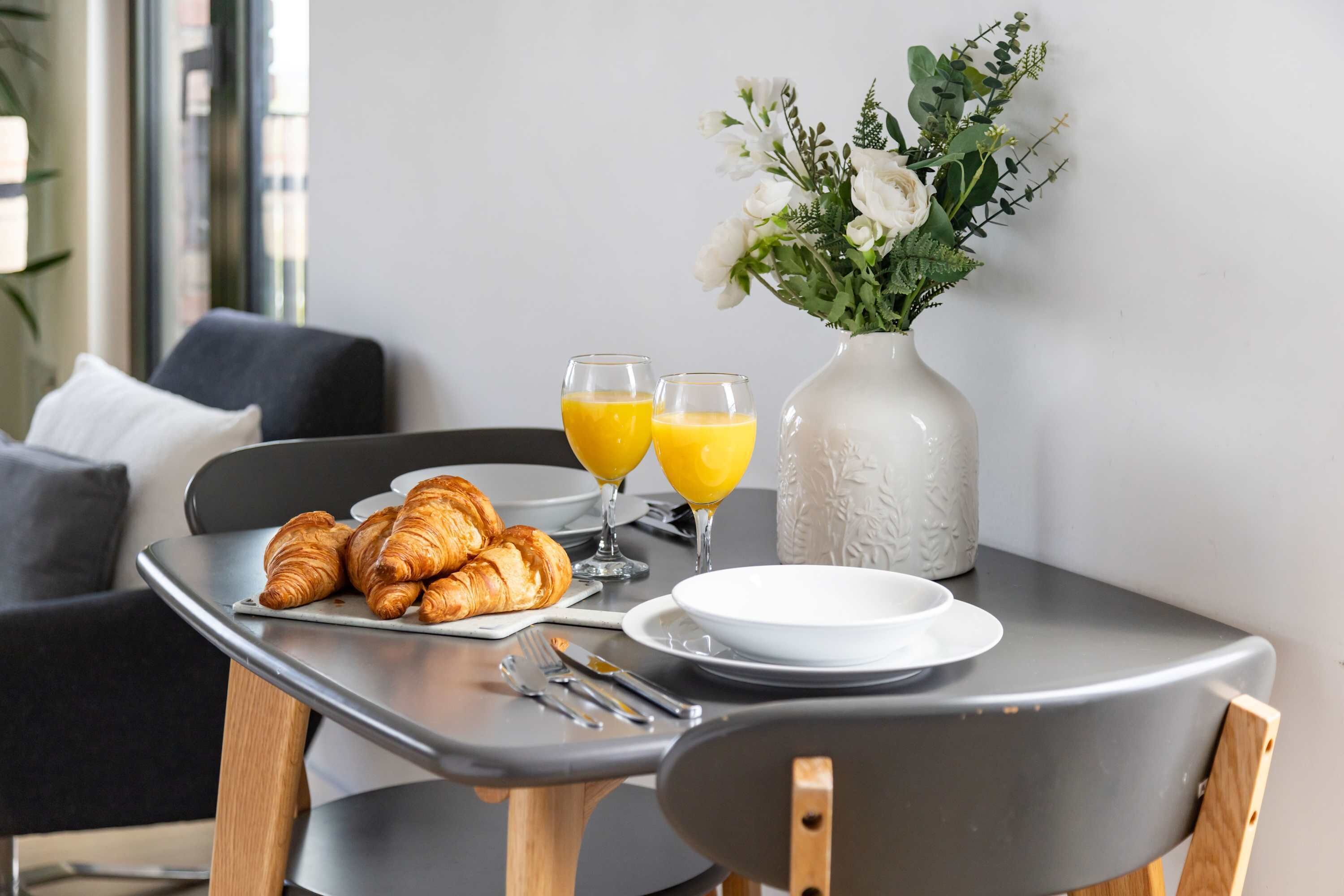 Ein Frühstückstisch mit Croissants, Orangensaft und einer Blumenvase.