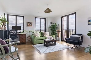 A spacious living area with a green sofa, a black armchair, a wooden coffee table, and a large window providing a view of the sky. - Bright 1BR with City Views by King's Cross (London)