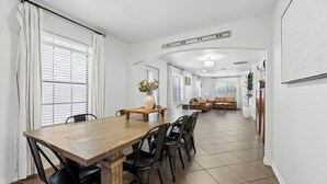Ein Essbereich mit Holztisch und Stühlen, einer Vase mit Blumen und einem Sofa im Hintergrund.