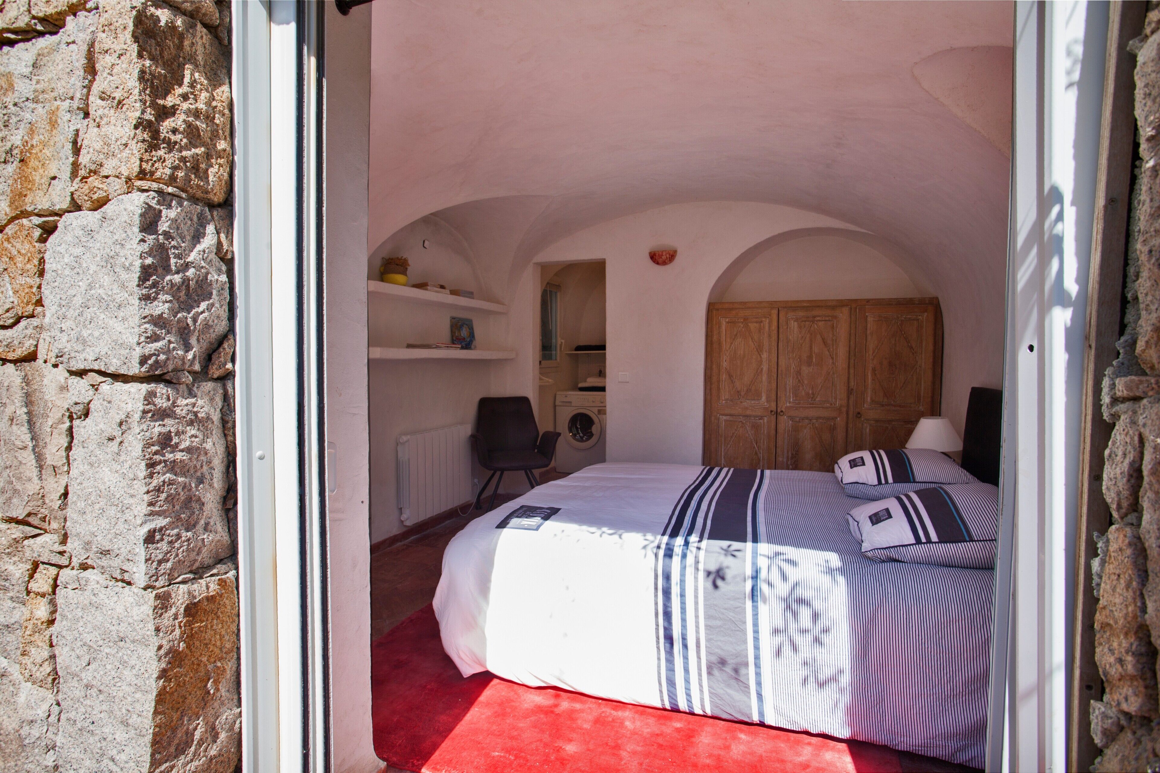 A bedroom with a bed, a wooden wardrobe, a chair, and a washing machine.