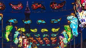Una strada ben illuminata, con decorazioni luminose e una torre sullo sfondo.