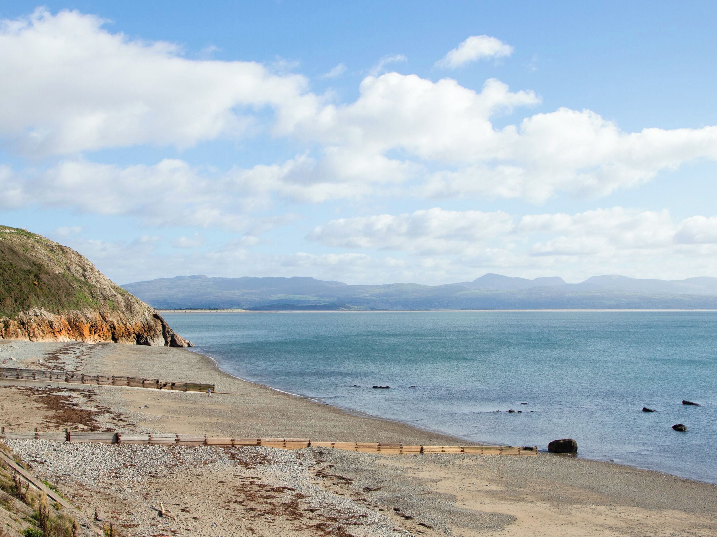 A coastal beach with a wooden walkway and rocky terrain.