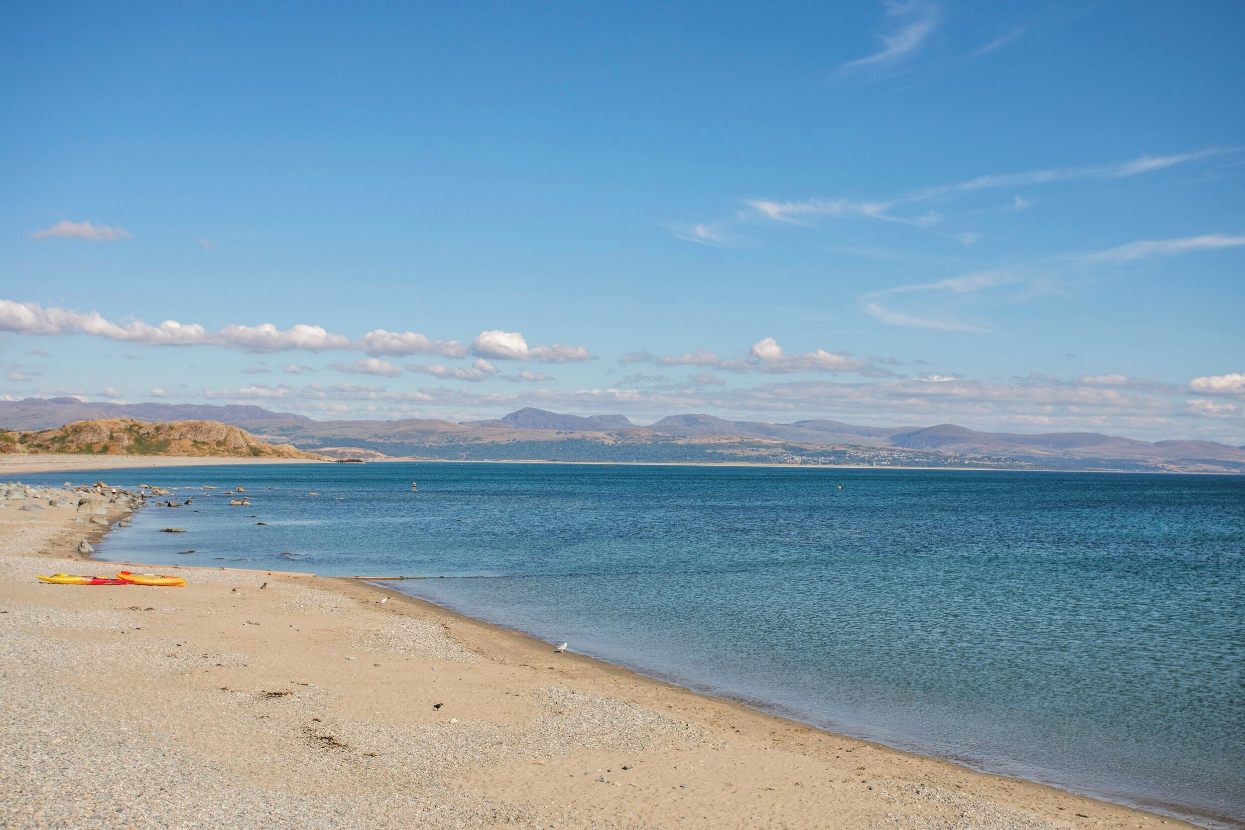 A beach with a kayak, calm water, and distant mountains.