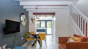 A modern living room with a flat-screen TV, a dining table with yellow chairs, a blue cabinet, and a staircase. - East Meets West (Criccieth)