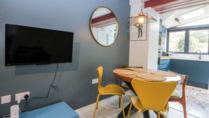A dining area with a round table, yellow chairs, a mounted TV, and a blue cabinet. - East Meets West (Criccieth)