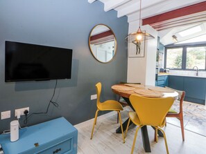 A dining area with a round table, yellow chairs, a mounted TV, and a blue cabinet. - East Meets West (Criccieth)