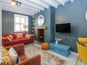 A living room with a red sofa, a blue cabinet, a yellow chair, a fireplace, and a mounted TV. - East Meets West (Criccieth)