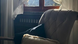 Ein Zimmer mit Fenster, Heizkörper und einem Sessel mit Kissen.