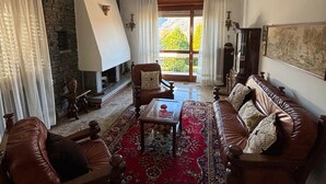 Ein Wohnzimmer mit Kamin, Ledersofas, einem Couchtisch und einem großen Fenster mit Vorhängen.