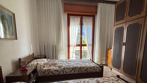 Ein Hotelzimmer mit zwei Betten, einer Chandelüster, einem Fenster mit Vorhängen und Blick nach draußen.