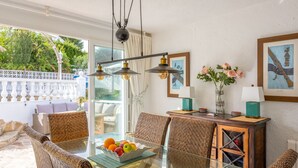 A dining area with a glass table, wicker chairs, a fruit bowl, and a wooden cabinet with a lamp. - Villa CATALINA by Abahana Villas (Teulada)