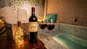 Una botella de vino Chateau Margaux, dos copas de vino tinto, una vela y una bañera en una habitación con paredes de piedra.