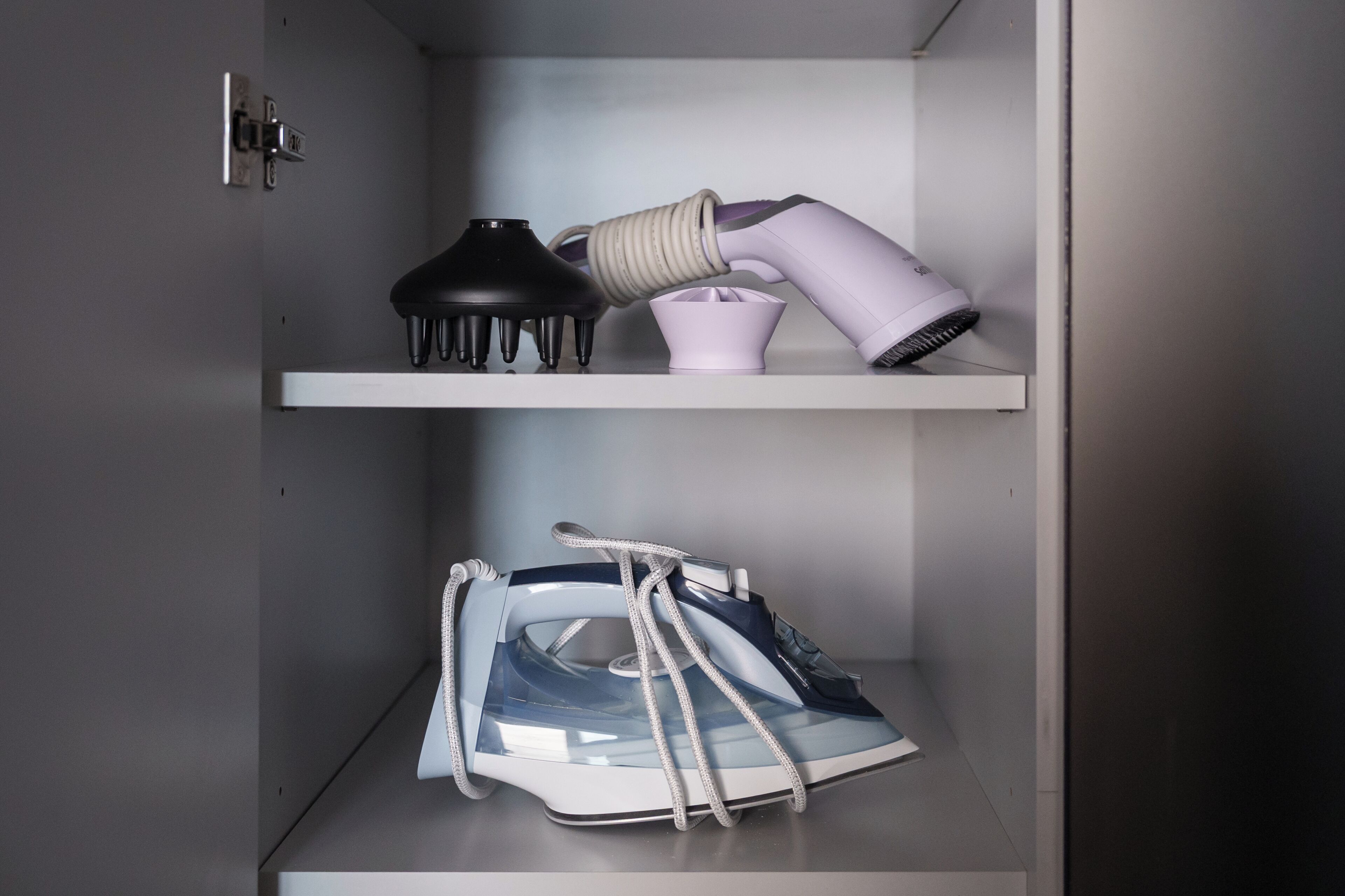 A storage unit with shelves containing a hairdryer, a vacuum cleaner, and a pair of shoes.