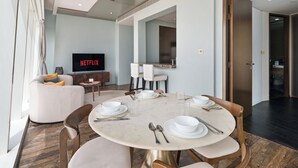 A modern dining area with a round table set for four, a sofa, a TV displaying 'NETFLIX,' and a mirror above the table. - Prime 2BR in Damac Heights Marina (Dubai)