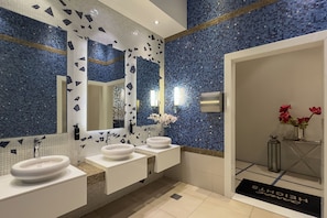 Ein modernes Badezimmer mit Mosaikfliesen, drei weißen Waschbecken und einem großen Spiegel.