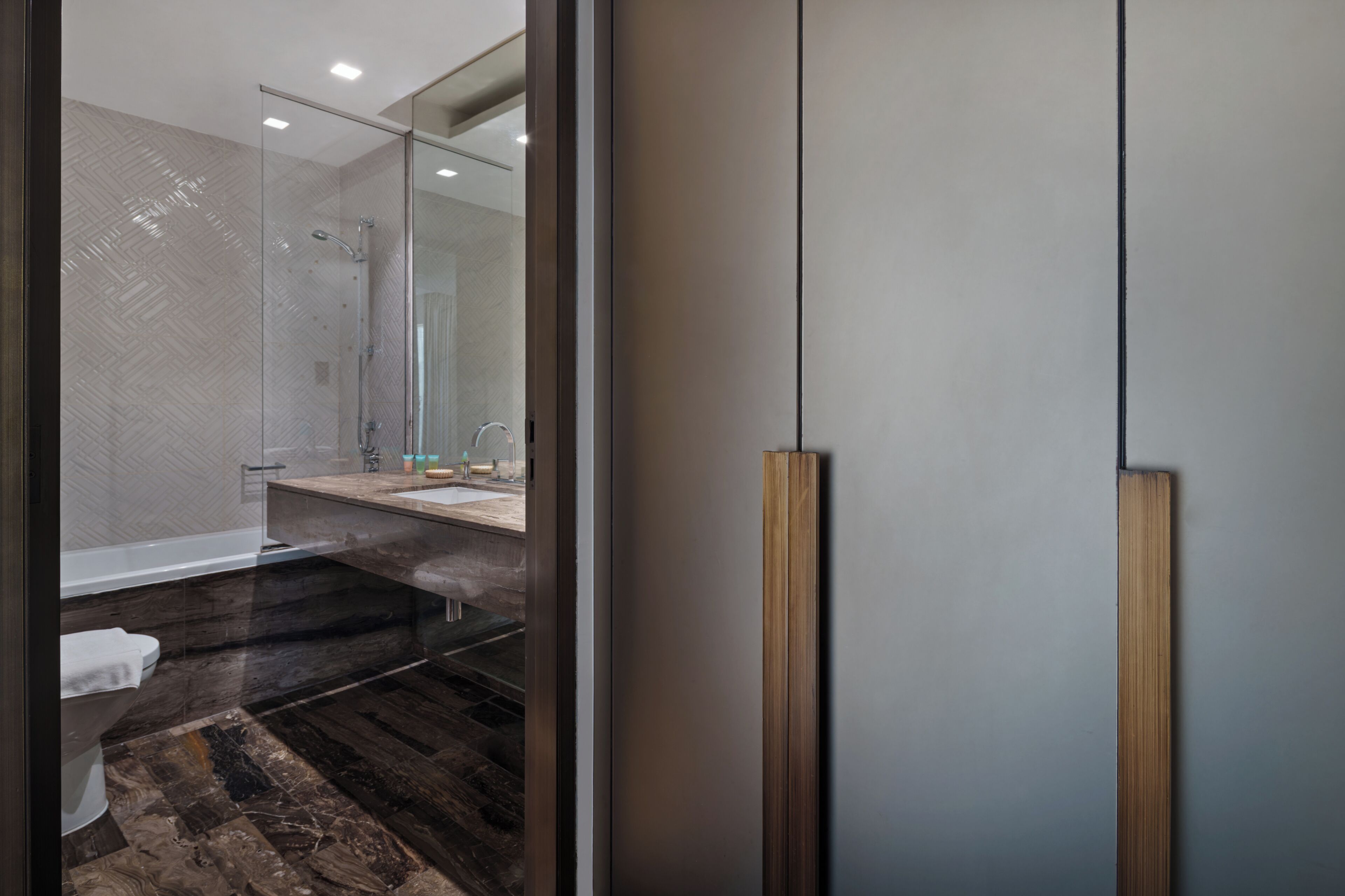 Un baño moderno con cabina de ducha de vidrio, suelo de madera y un espejo grande.