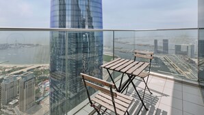 A high-rise building with a glass facade, a view of a river, and a wooden bench on a balcony. - Prime 2BR in Damac Heights Marina (Dubai)