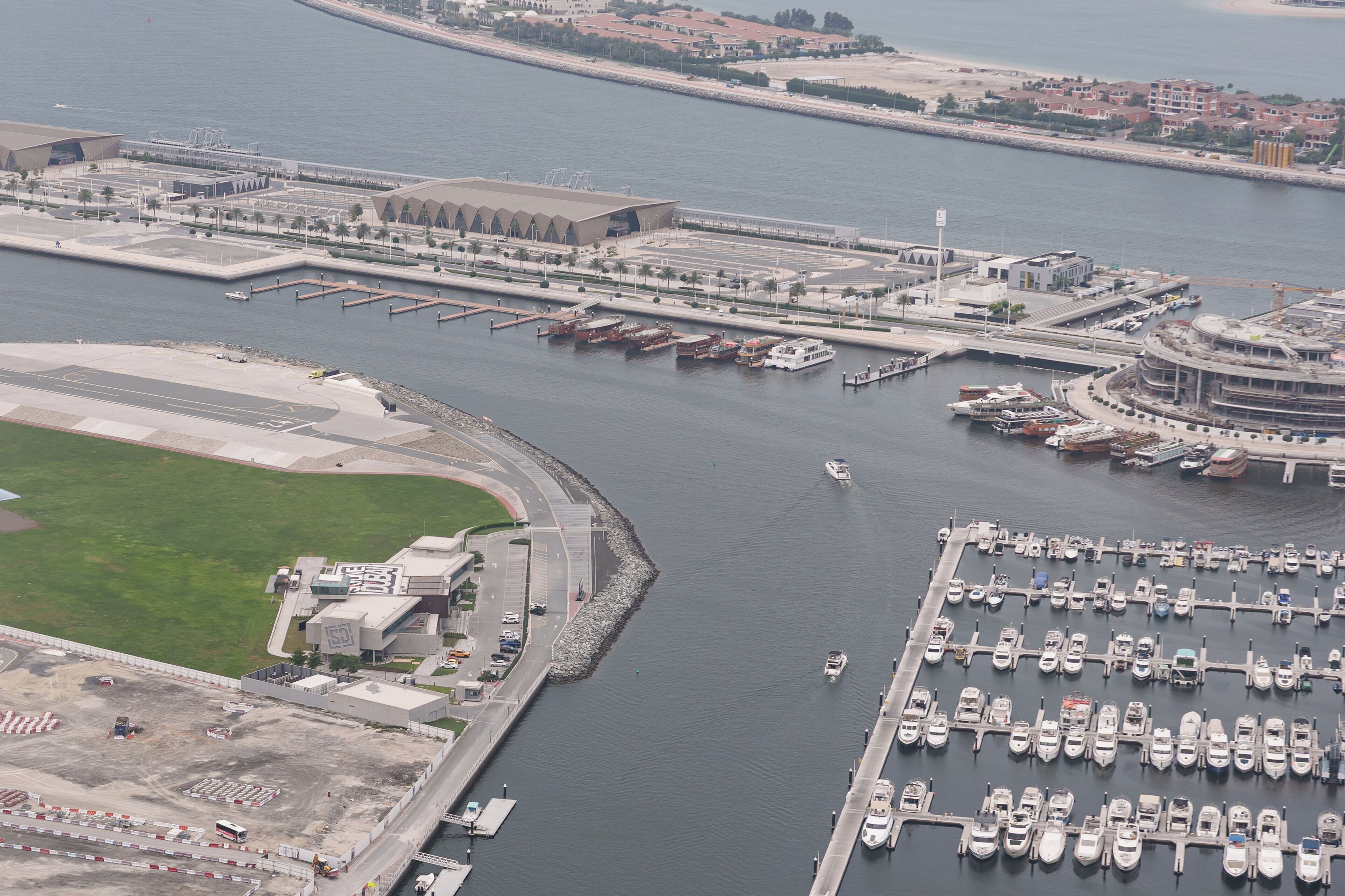An aerial view of a marina with boats docked, a large building with a unique architecture, and a road leading to the marina.