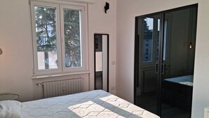 Ein Schlafzimmer mit einem Bett, einem Fenster, einer Heizung, einem Spiegel und einer Schiebetür, die auf einen Balkon führt.