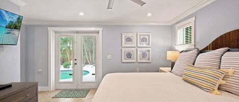 A bedroom with a bed, a ceiling fan, a TV, a door leading to a pool, and framed artwork on the wall.