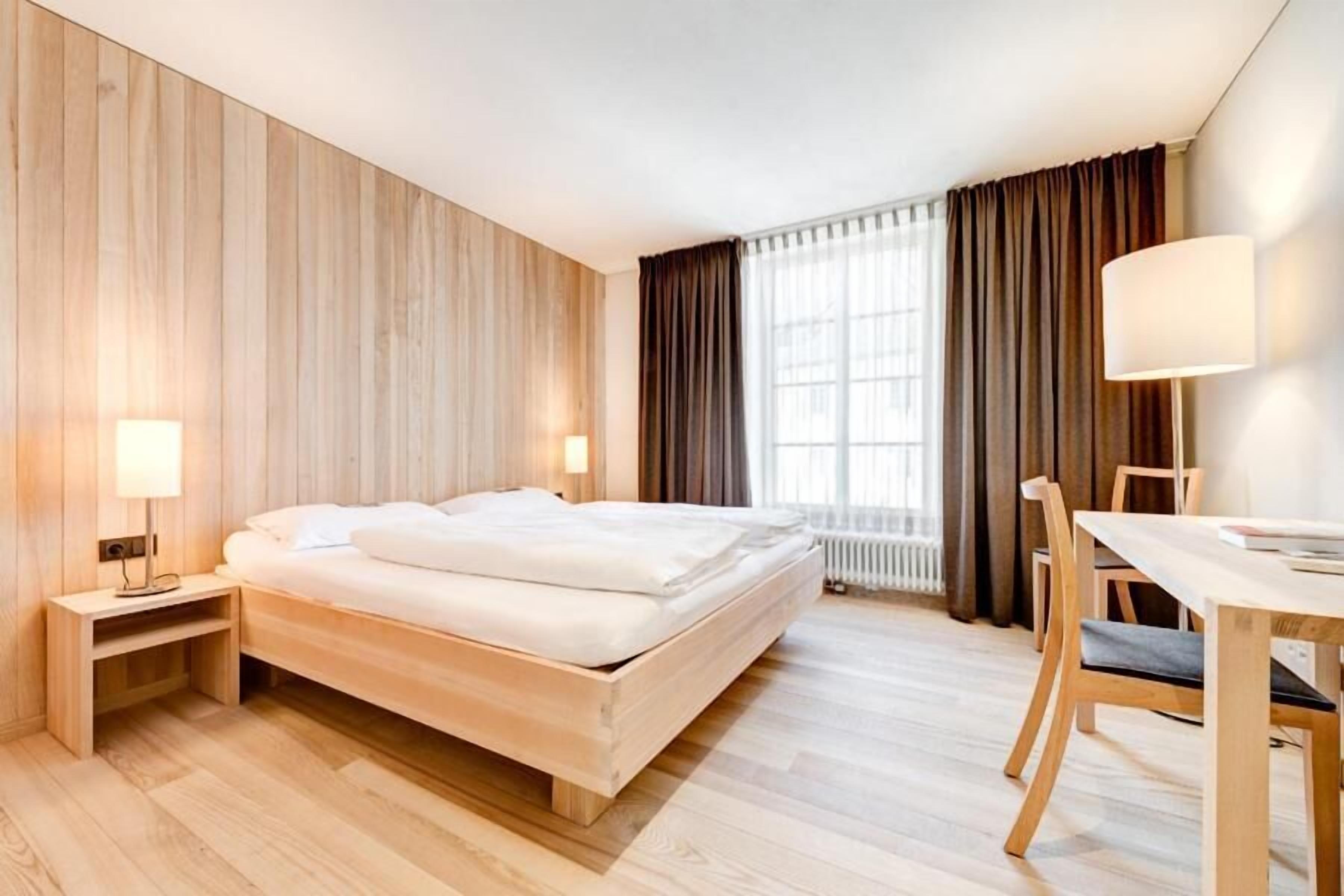 Une chambre d’hôtel avec un lit en bois, une table de chevet, une lampe et un coin repas comprenant des chaises et une table.