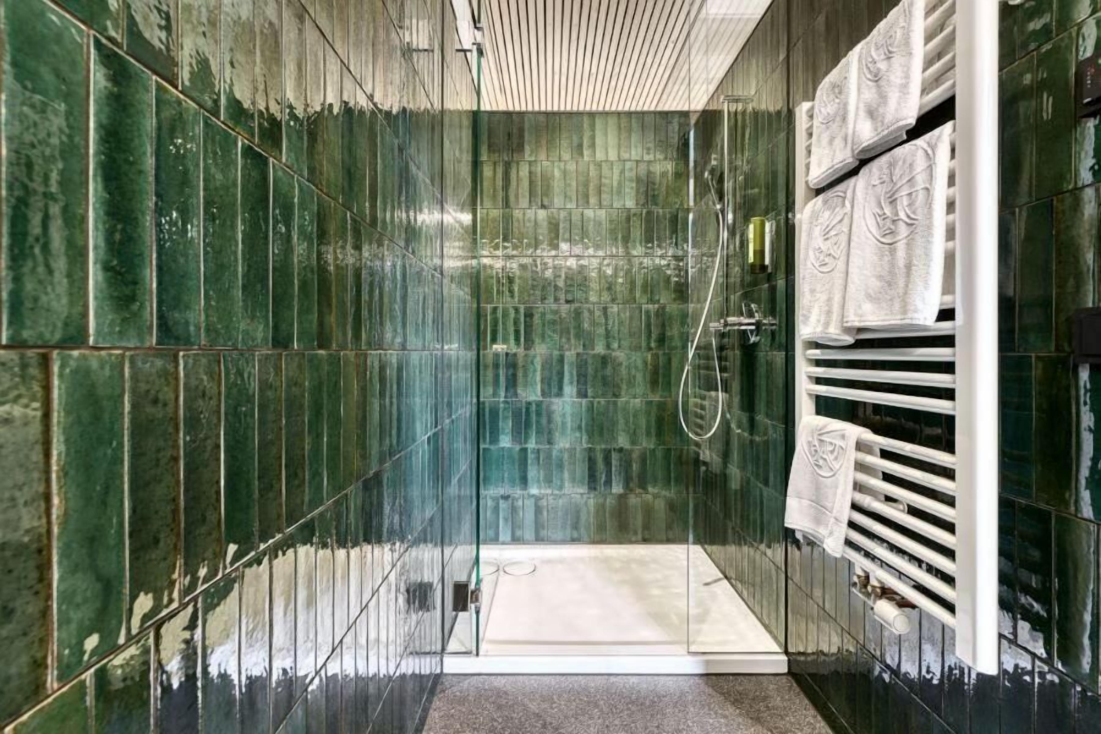 Une salle de bain moderne avec une douche à parois de verre, un porte-serviettes blanc et des murs recouverts de carreaux verts.