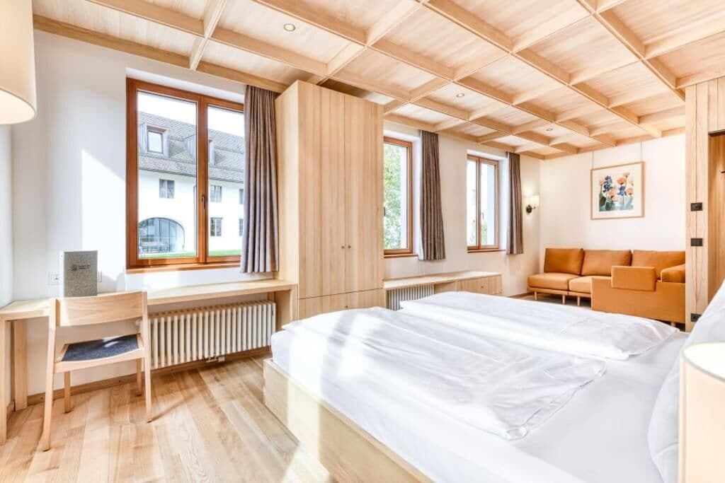 A modern hotel room with a large bed, wooden ceiling, and a view of the outside.