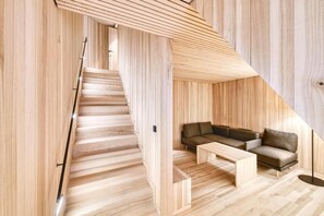 Um interior moderno com escada de madeira, sofá e mesa de centro.