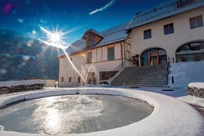 Un edificio cubierto de nieve con una fuente, una escalera y el paisaje de una montaña al fondo.