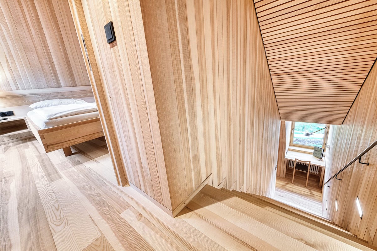 A wooden interior with a bed, a desk, and a window.