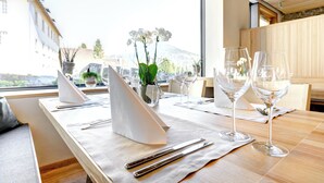 Una mesa de comedor con cubiertos, un jarrón con flores blancas y copas de vino.