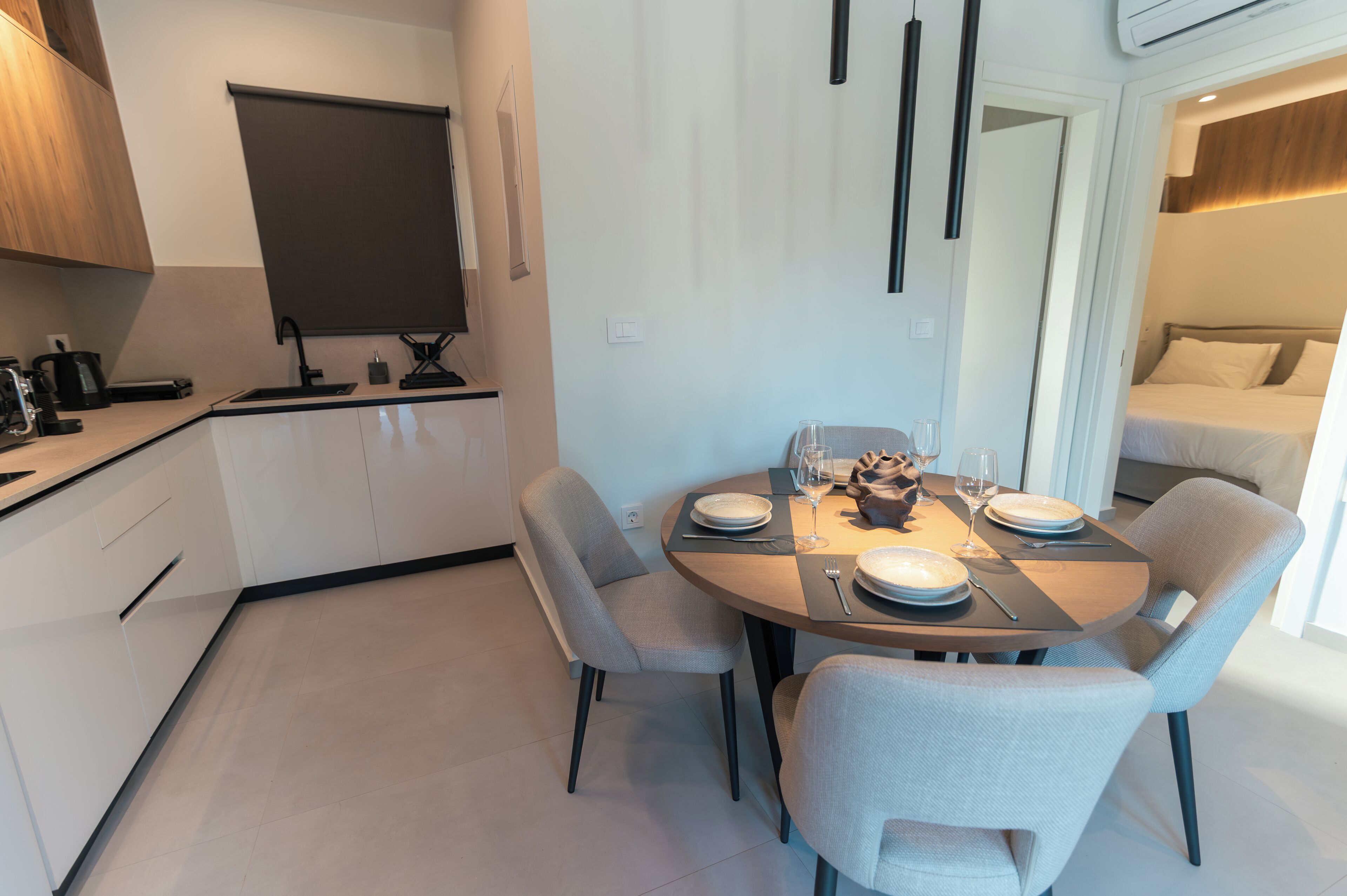 Una cocina moderna con comedor, que incluye una mesa preparada para cuatro personas, horno empotrado y ventana con persiana.