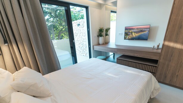 A bedroom with a bed, a desk, a TV, and a view of the outdoors.