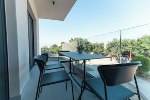 A balcony with a table and chairs, a potted plant, and a view of trees and buildings. - Avli Residences (Kos)